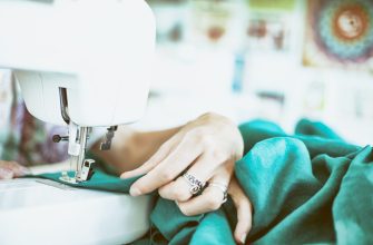 person sewing green textile using white electric sewing machine
